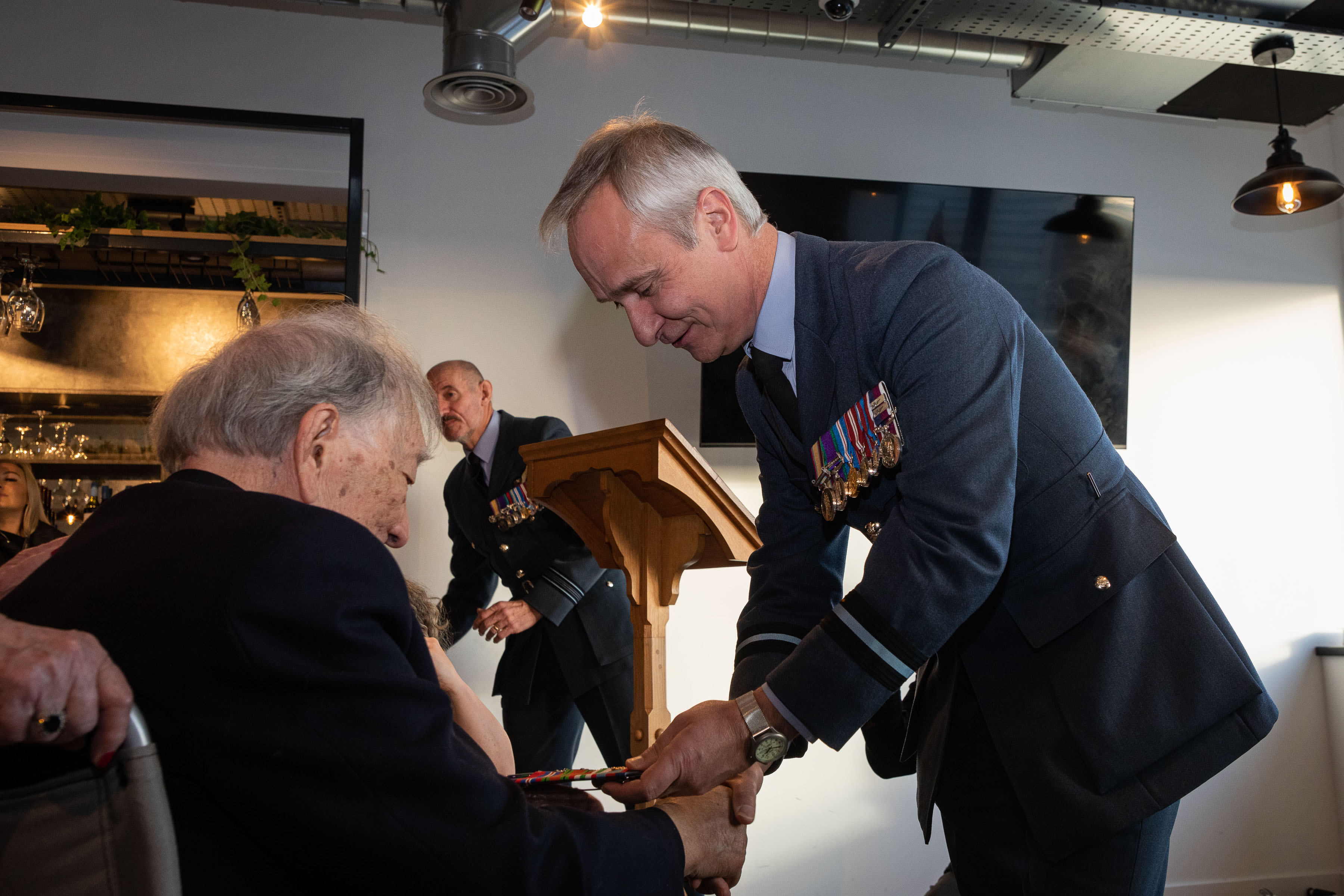 Image shows RAF aviator shaking hands with veteran.